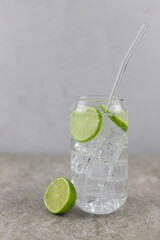 Refreshing drink, water with ice and lime on a gray background.