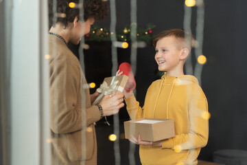 Happy teenage boy in hoodie receiving bluetooth speaker in gift from mother on Christmas