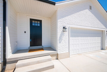 Facade of a house with white exterior and black front door with glass, doorbell camera and lockbox