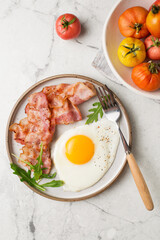 English breakfast. Egg and fried bacon. A cup with tomatoes. Serving breakfast on a marble table. Fried egg.