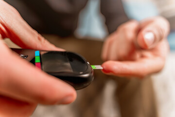 A man at home uses a glucose meter to measure blood glucose. Piercing a finger with a needle