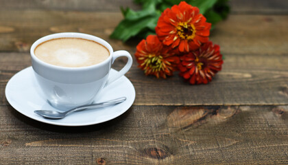 Close up white coffee cup with foam on brown wood table near to flowers, quote space, note, creative concept