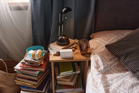 Image of bed table with modern alarm clock and books under the table near the bed in the bedroom