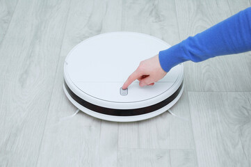 Caucasian woman presses her finger on  button on the cleaning robot vacuum cleaner.
