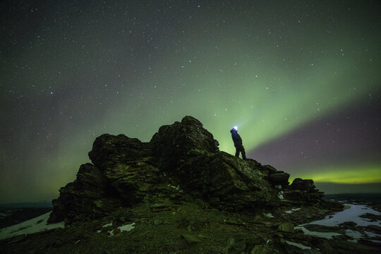 A person wearing a headlamp in silhouette, atop a rock with the aurora borealis in the background near Fairbanks, Alaska. 