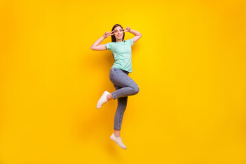 Fototapeta na wymiar Full size photo of crazy brunette hairdo millennial lady jump v-sign wear t-shirt jeans sneakers isolated on yellow background