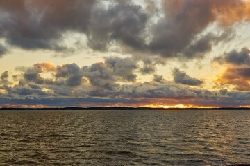 A colorful sunset on the Baltic Sea with clouds illuminated by the sun setting over the horizon.