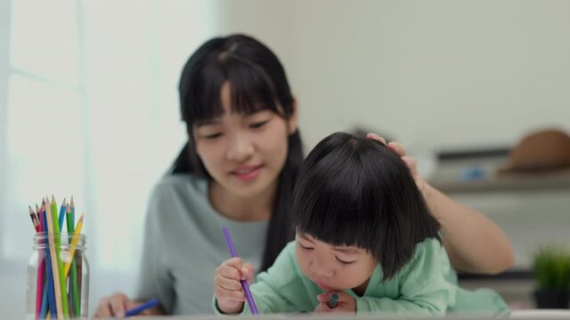 Happy asian boy painting with crayon and colored pencil with his mother in living room at home. Mom teaching son how to painting with crayon color on book or doing homework. family concept.