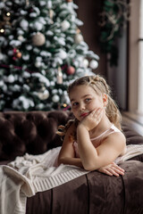 Portrait of a cute girl dreaming about gifts under the Christmas tree. Concept for family celebrating new year and christmas at home during coronavirus pandemic