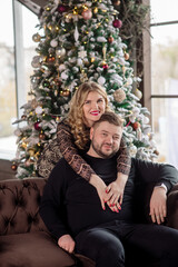 Obraz na płótnie Canvas Portrait of a young adult couple by the Christmas tree at home. Concept of family celebrating new year and christmas at home during coronavirus pandemic. Young man and woman hug.