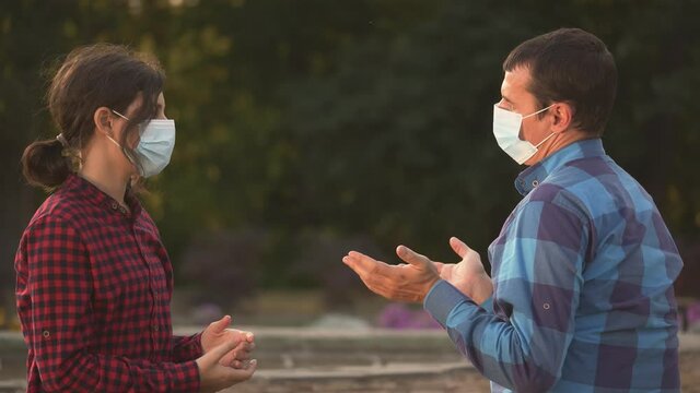 New Talking Of People At Distance In Medical Mask.two People, Man, Girl, Are Sitting On Park Bench, Talking In Medical Mask.talking Of Man, Girl In Park From Distance.talking Concept, Virus Safety