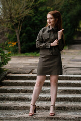 Attractive girl in a dark green suit standing in the park. Outdoor female portrait.