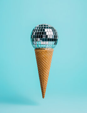 Party composition with ice cream cone and shiny disco ball on pastel blue background. Creative birthday or Christmas celebration concept. Minimal sweet food surreal advertisement idea.