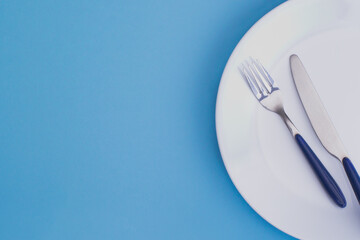 White dinner plate with fork and knife on blue