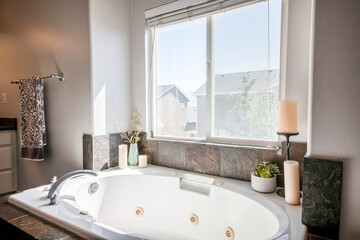 Bathtub with deck mounted faucet and rough stone tiles surround against the window