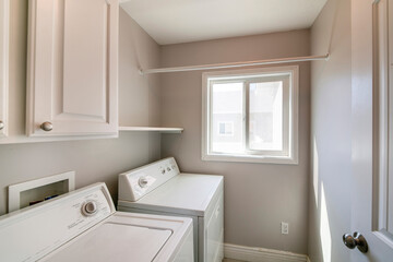 Fototapeta na wymiar Laundry room interior with light gray wall and white cabinets and laundry units