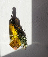 Rosemary oil bottle in sunlight, rosemary branch on white background