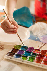 a child's hand dips a brush into watercolor paints