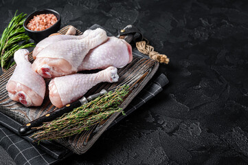Fresh Raw chicken drumsticks legs on wooden cutting board. Black background. Top view. Copy space
