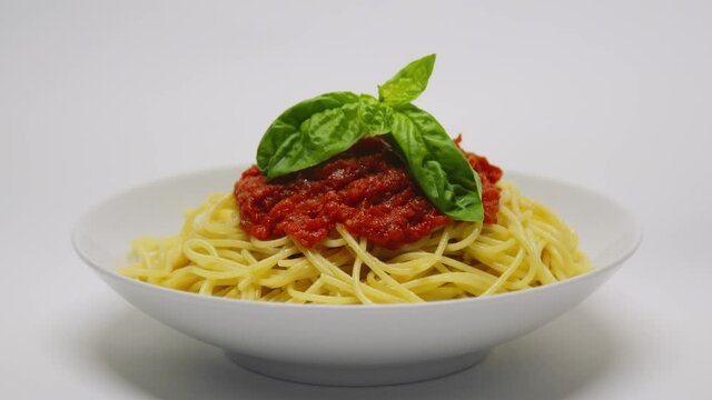 Una mano mette una foglia di basilico su un piatto di spaghetti al pomodoro