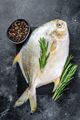 Raw fish pompano with herbs on a  marble board. Black background. Top view
