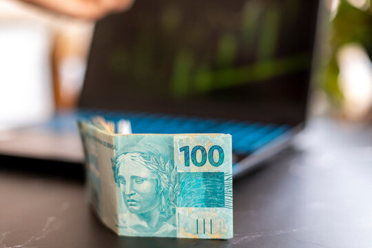 Brazilian money banknotes on the table, with blurred background of laptop computer