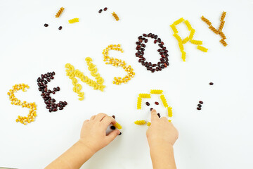 Sensory word written of popcorn, beans, pasta and children hands. Sensory play for child at home....
