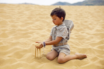 boy is a child traveler in a suit of an archaeologist tracker and wearing hat sitting on the sand...