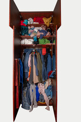 Isolated open wardrobe with clothes on hangers and clutter in open drawers. Open wardrobe with clothes on a white background