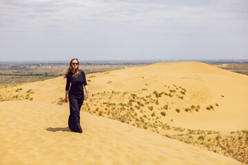 Fototapeta na wymiar woman in black long dress walks through the desert dunes in summer with her back