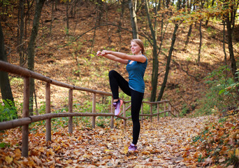 Young slim woman doing fitness exercise stretching in autumn forest park background, active healthy lifestyle outdoors