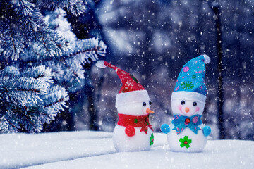 Two snowmen in the woods near a spruce tree during a snowfall. Christmas and New Year card