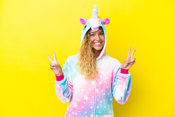 Girl with curly hair wearing a unicorn pajama isolated on yellow background showing victory sign...