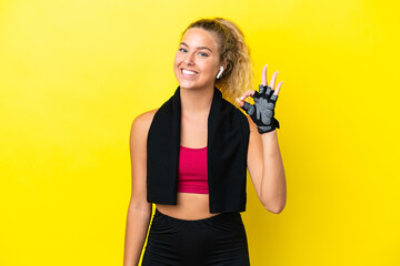 Sport woman with towel isolated on yellow background showing ok sign with fingers