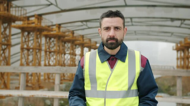 Ambitious engineer is putting on protective helmet and crossing arms standing in industrial area alone and looking at camera. Job abd specialists concept.