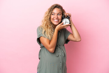 Fototapeta premium Girl with curly hair isolated on pink background pregnant and holding clock