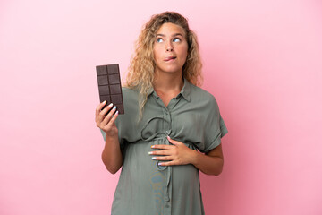 Girl with curly hair isolated on pink background pregnant and holding chocolate with hungry