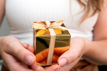 Woman holding a golden gift box in a gesture of giving. Mothers Day,Christmas,Birthday present concept pastel natural color background