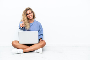 Girl with curly hair with a laptop sitting on the floor showing and lifting a finger