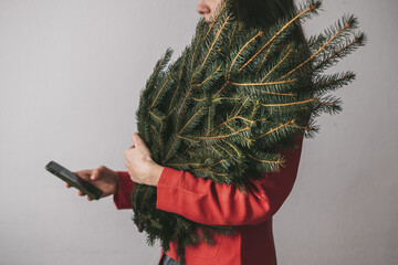 Female holding spruce branches and hands with smartphone texting message or dialing number on a...