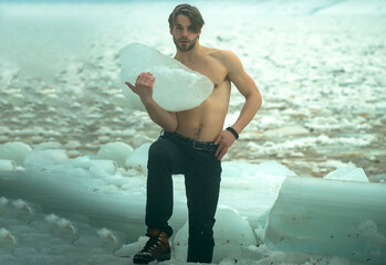 Sexy gay man with muscular bare chest hold frozen cracked ice block in cold winter, power and...