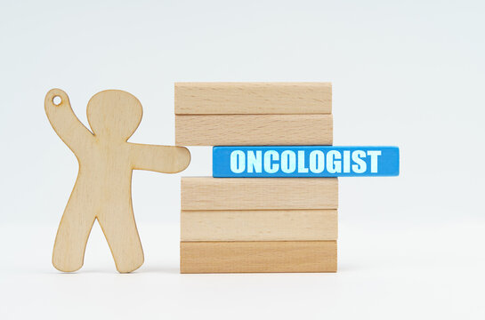 A human figurine pushes a blue wooden block labeled - ONCOLOGIST from a wall of blocks.