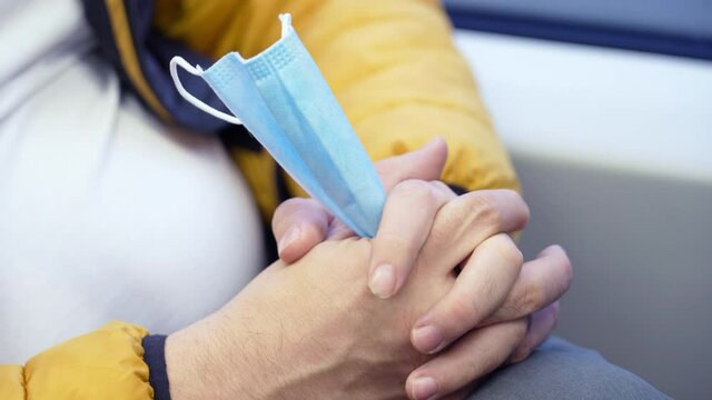 Close-up of nervous convulsive movements of fingers holding a medical mask. A man is riding on a train and nervously clutches a medical mask in his hands on his knees