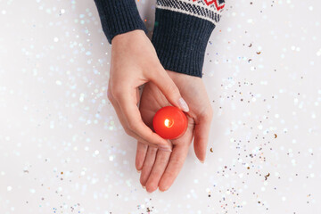 Female hands in sweater holding red candle with flame. Winter holiday, Christmas, Valentine's day background. Giving warm and love concept. Xmas backdrop for design projects, postcards. New Year theme