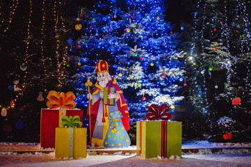 Beautiful big Christmas tree in the city, under which stands the figure of wooden St. Nicholas with...