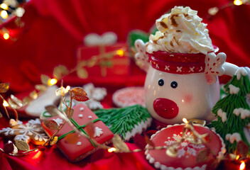 Banner for Christmas and New Year gingerbread cookies snowflakes, Santa hat, Christmas trees, garlands and mug with hot chocolate and cream on red silk fabric background