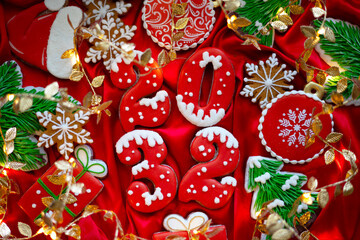 Banner for Christmas and New Year gingerbread cookies numbers 2032, snowflakes, Santa hat, Christmas trees, garlands on red silk fabric background