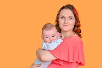Mom with an infant child on a yellow studio background. A woman holds a baby four months old in her arms