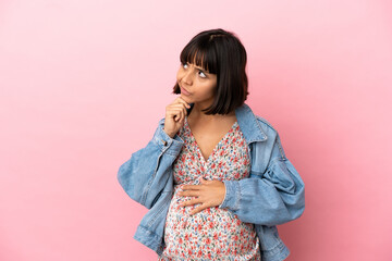 Young pregnant woman over isolated pink background and looking up