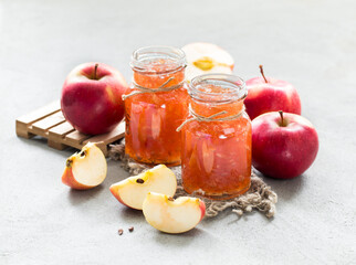 Apple jam in a glass jar on a linen napkin on a light gray background in rustic style